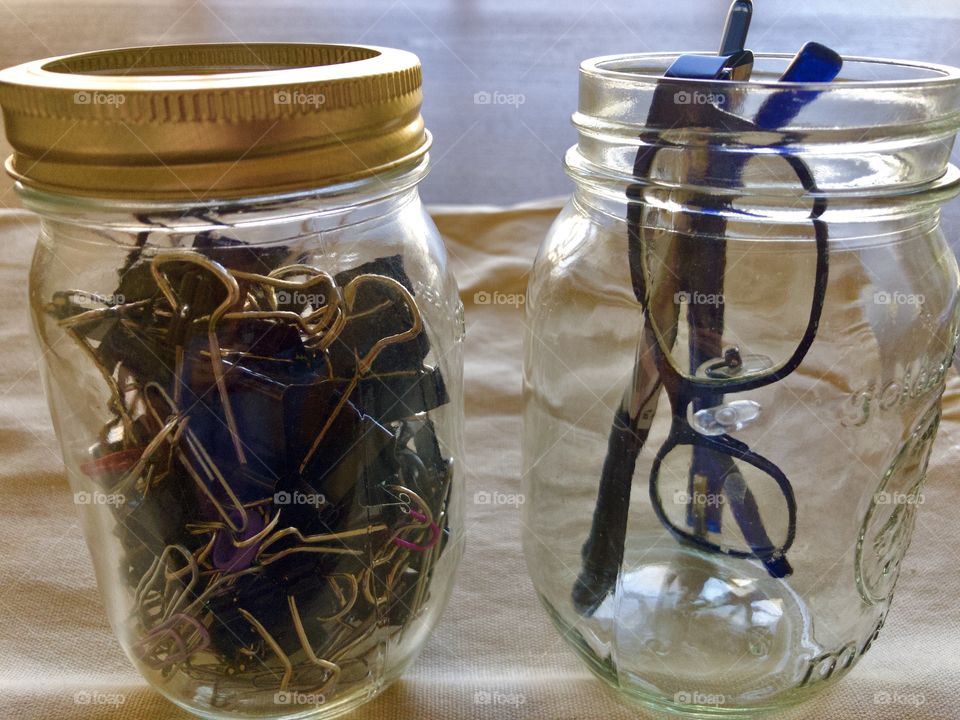 Two glass jars on desk holding glasses and binder clips