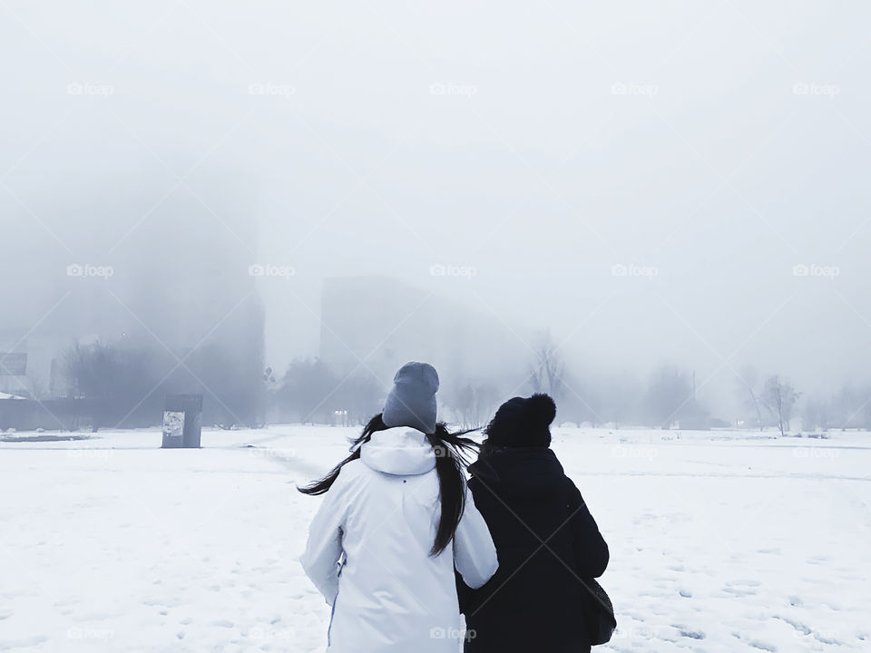 Two people walking together through the misty city during the winter foggy weather 