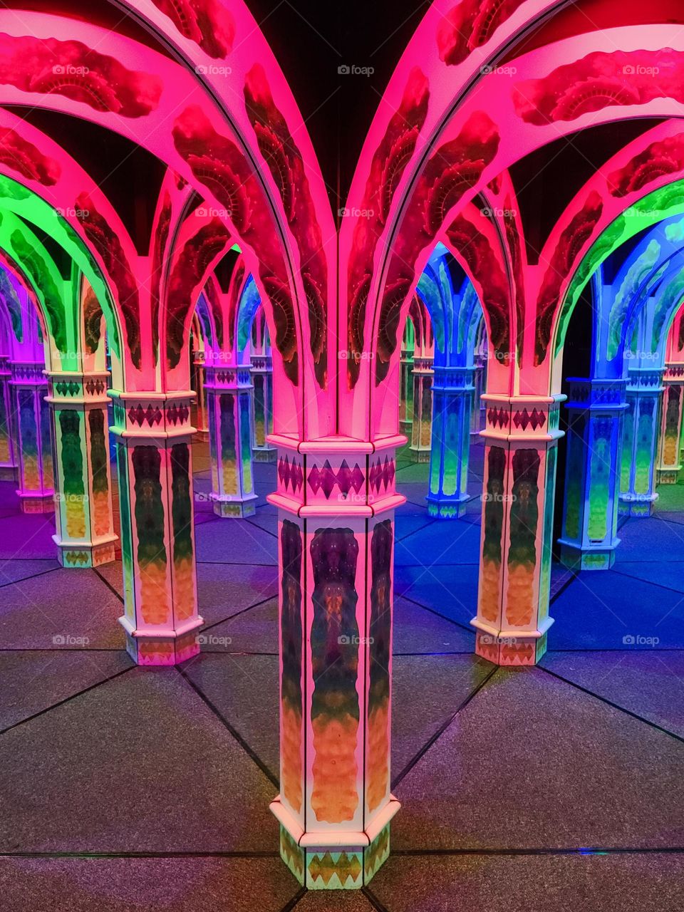 Hall of mirrors with arches lit up and reflecting the colors of the rainbow giving the allusion of a vast space 