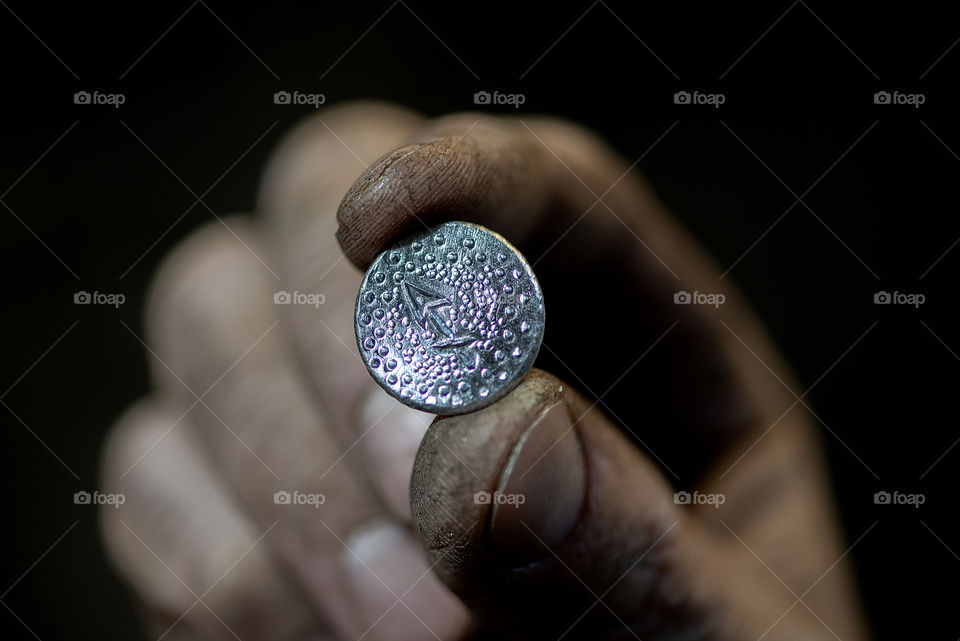 Close-up of blacksmith fingers hold coin