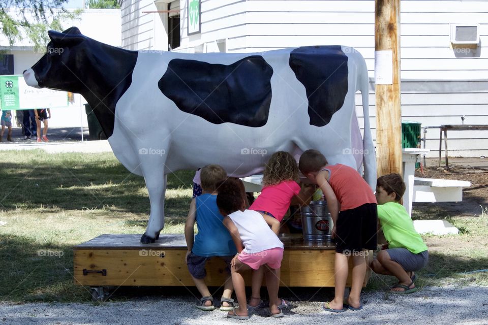 Little children, excited about learning how to milk a cow, take turns practicing on a dairy cow milking simulator