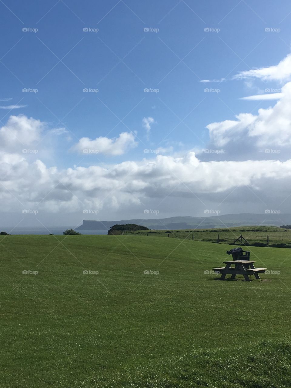 A large, empty field in Ireland with the ocean and cliffs in the background. And there’s one line bench in the middle of the field 