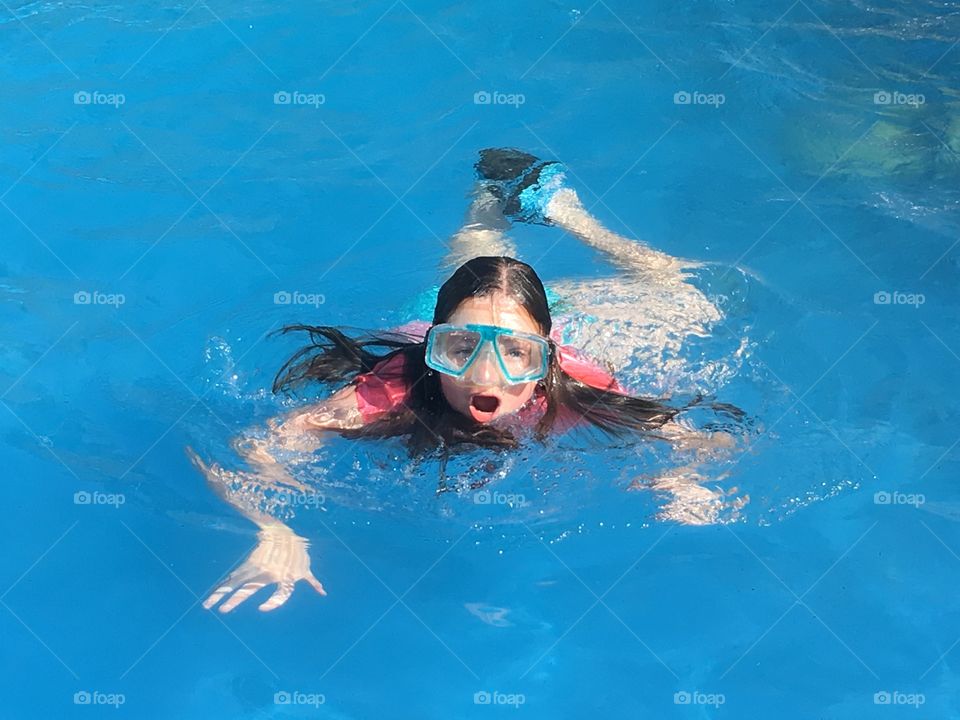 Ten year old girl in snorkel mask and flippers swimming alone in swimming pool, holiday fun!