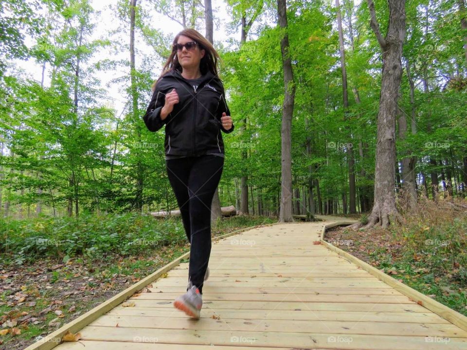 Female jogging on boardwalk in park with trees