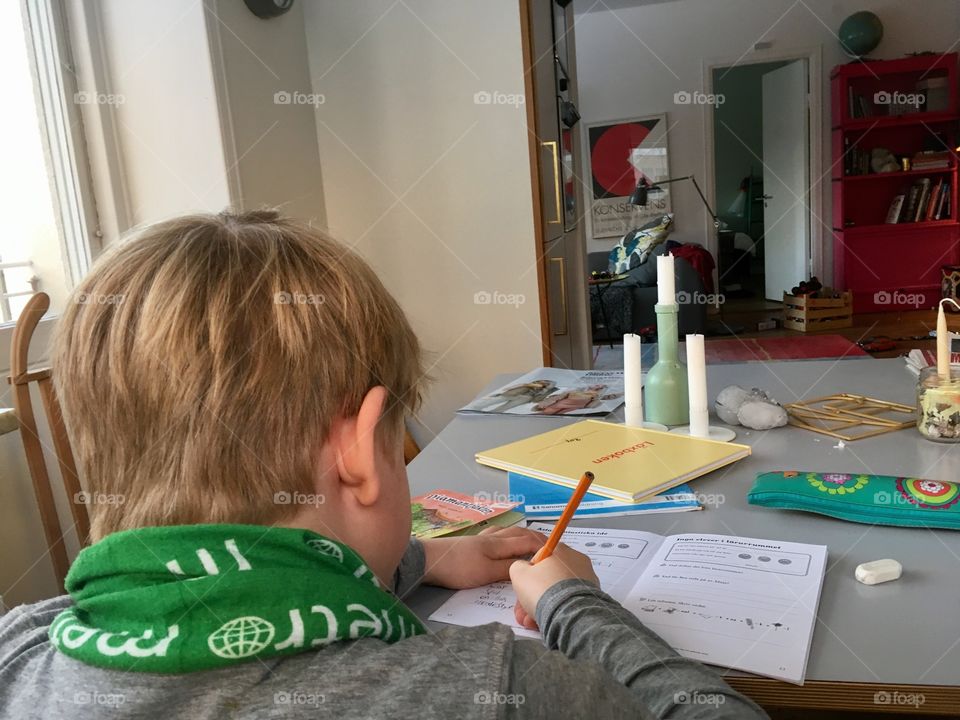 Boy doing homework in kitchen, from behind 