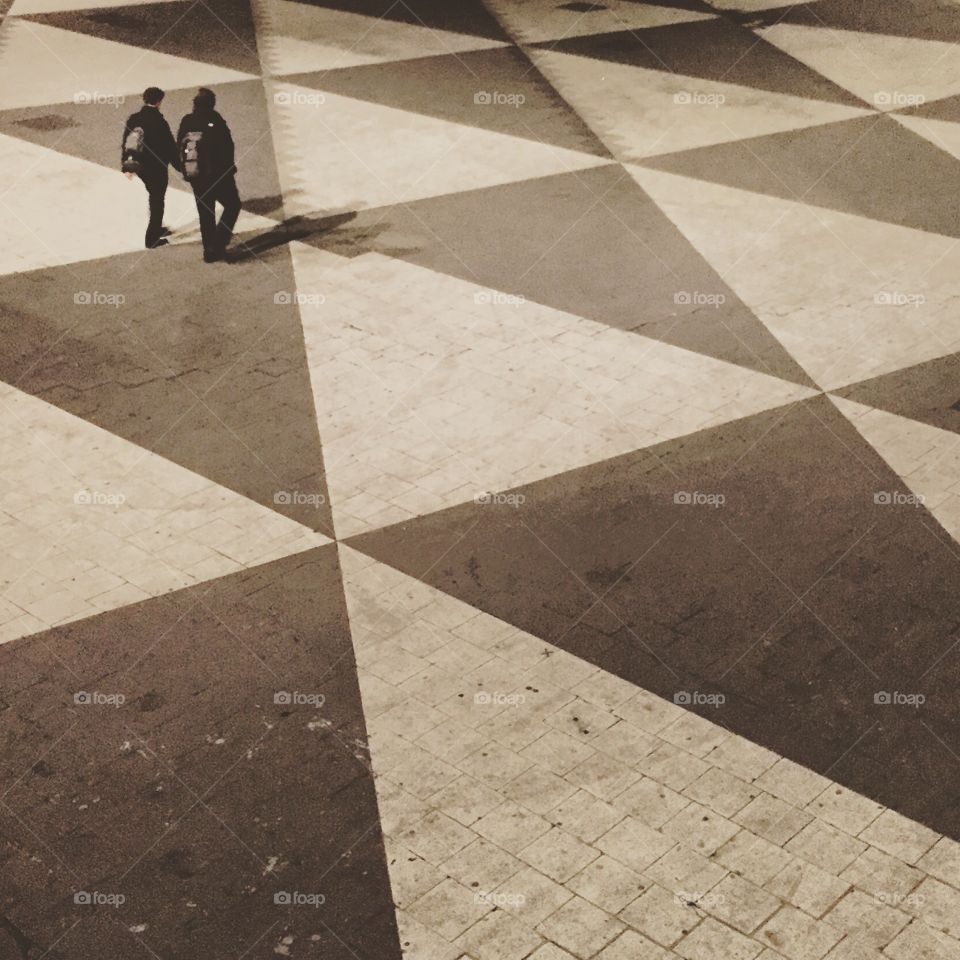 Across the square. Two people walking across triangle-ornamented square