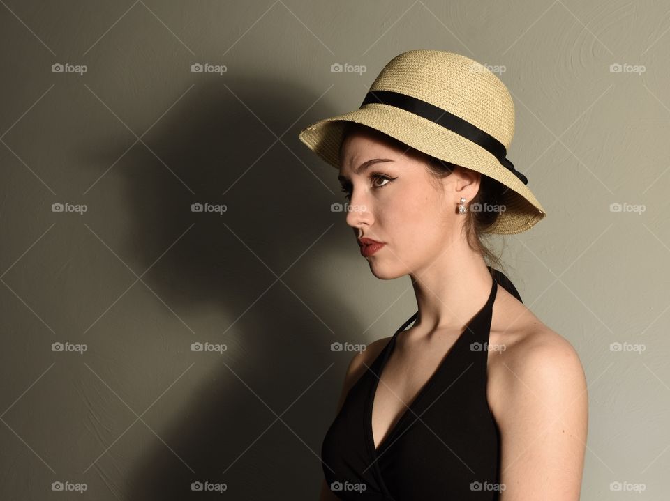 Beautiful woman in a black dress wearing a hat with her shadow against the wall