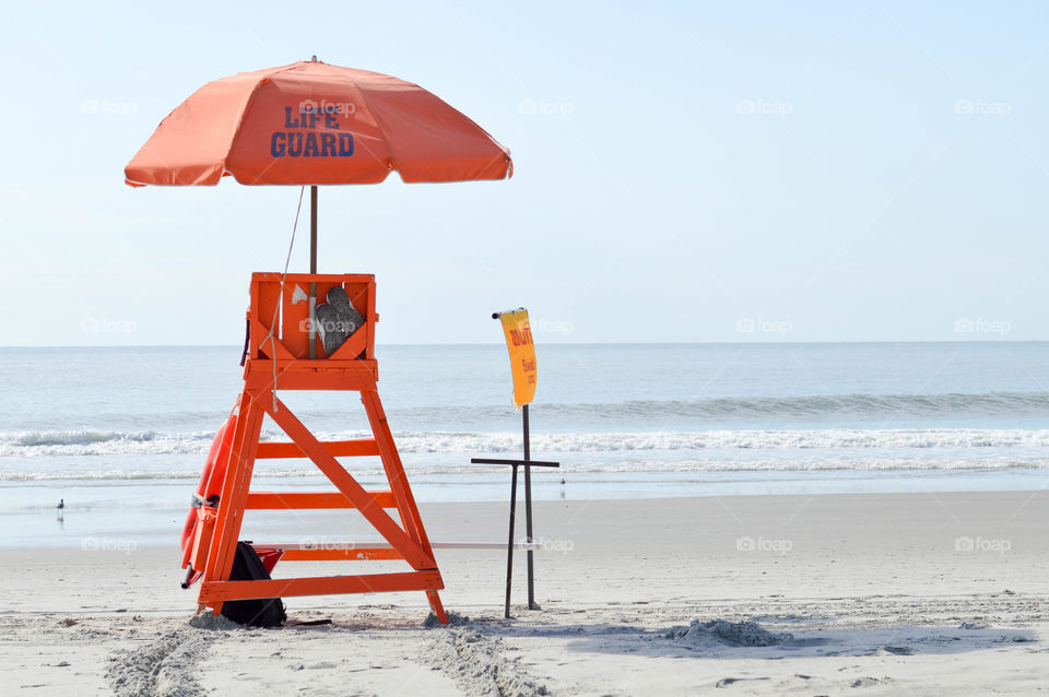 Empty, orange lifeguard chair with umbrella on the beach with no people