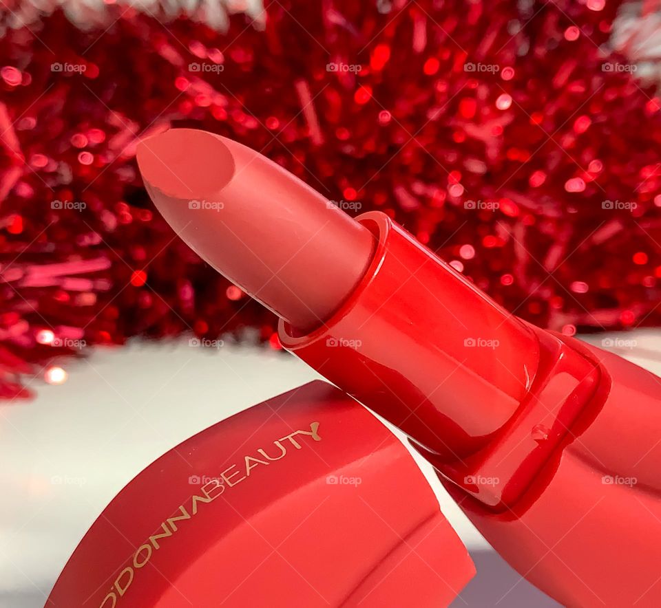 Red lipstick in a lip shaped container with a red tinsel background 