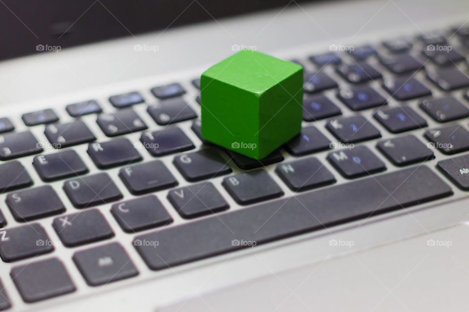 Green wooden block on top of laptop keyboard. Focus concept