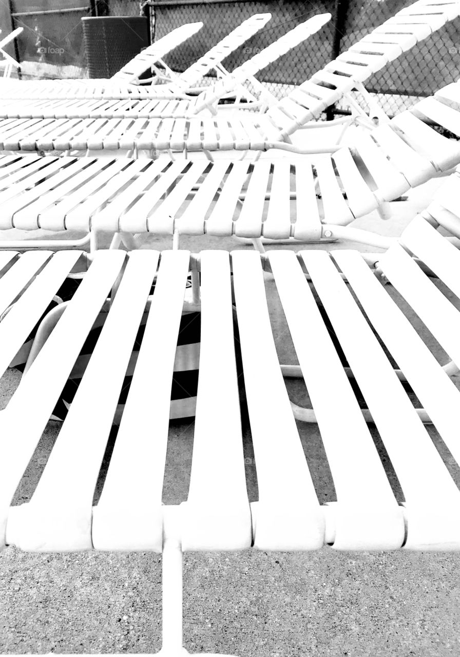 Black and white photo of lawn chairs lined up at pool just waiting for people to come and enjoy the relaxation they offer. 