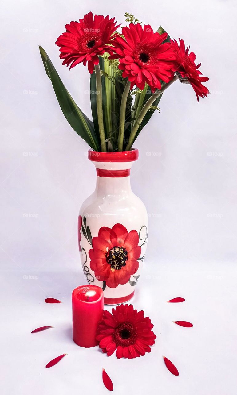 red flowers in a vase, with a candle and a little flower, on a white background