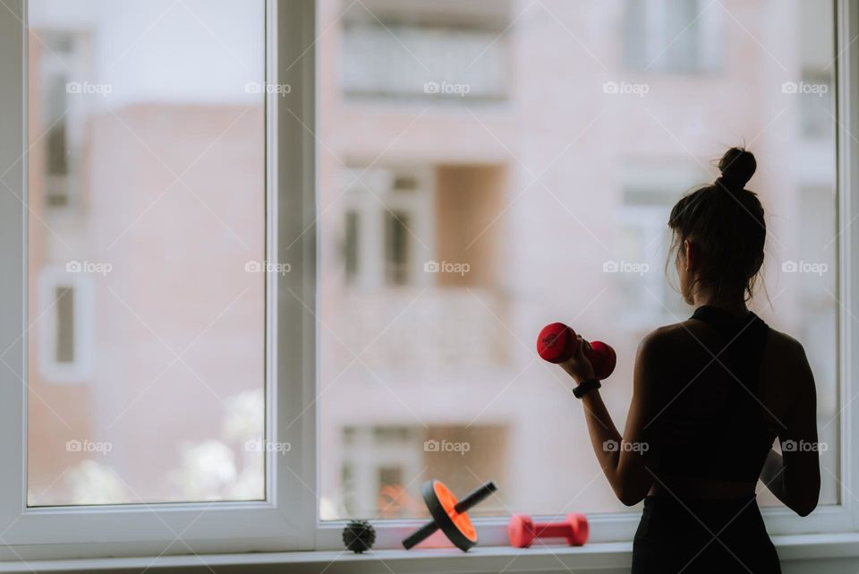 Young woman working out at home lifting weights near a window