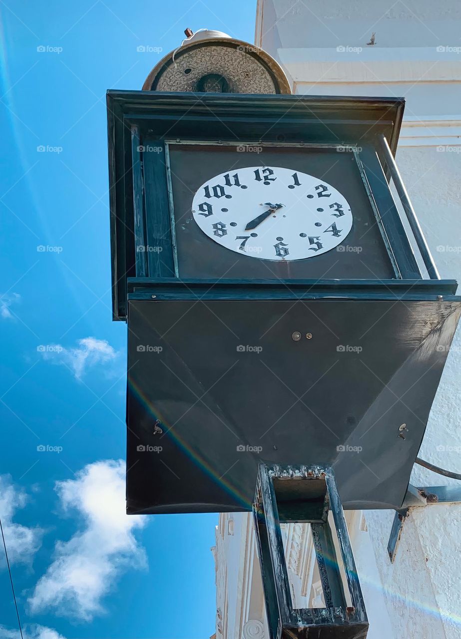 Large cube historical style black clock in downtown area in the old part of the town hanging on the corner wall from a corner street architectural and historical building.