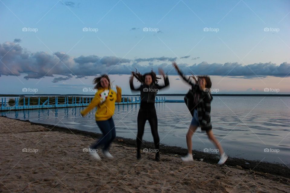 Three girls are jumping against the background of the evening landscape.