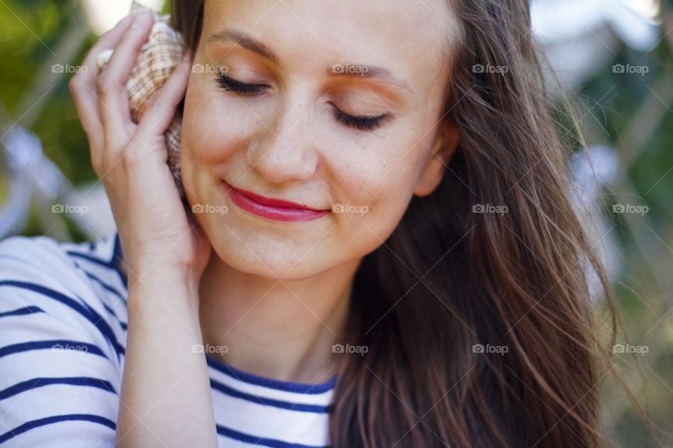 beautiful girl holding shell near her ear