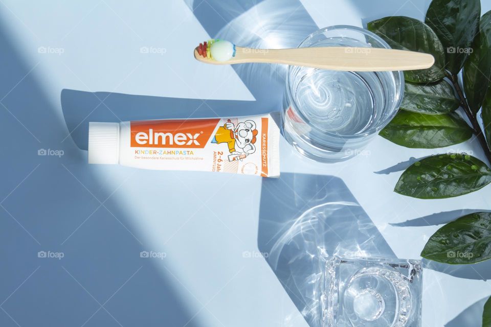 Elmex toothpaste for small children for oral and dental care, ecological toothbrush is on a blue background, with water, and a green flower.