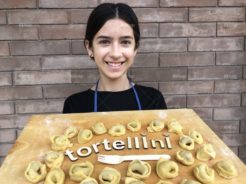 Young girl showing homemade tortellini, traditional italian filled pasta on a wooden board