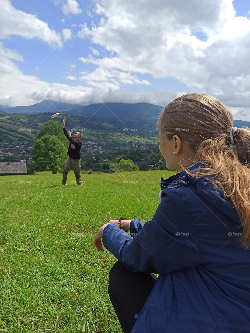 A girl looks at a Frisbee game in a meadow in the mountains. Carpathian.. Ukraine. Life goes on.