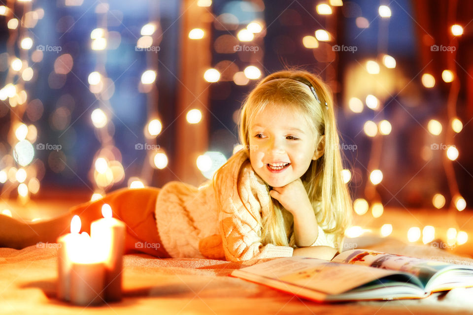 Cute little girl with blonde hair reading book at home
