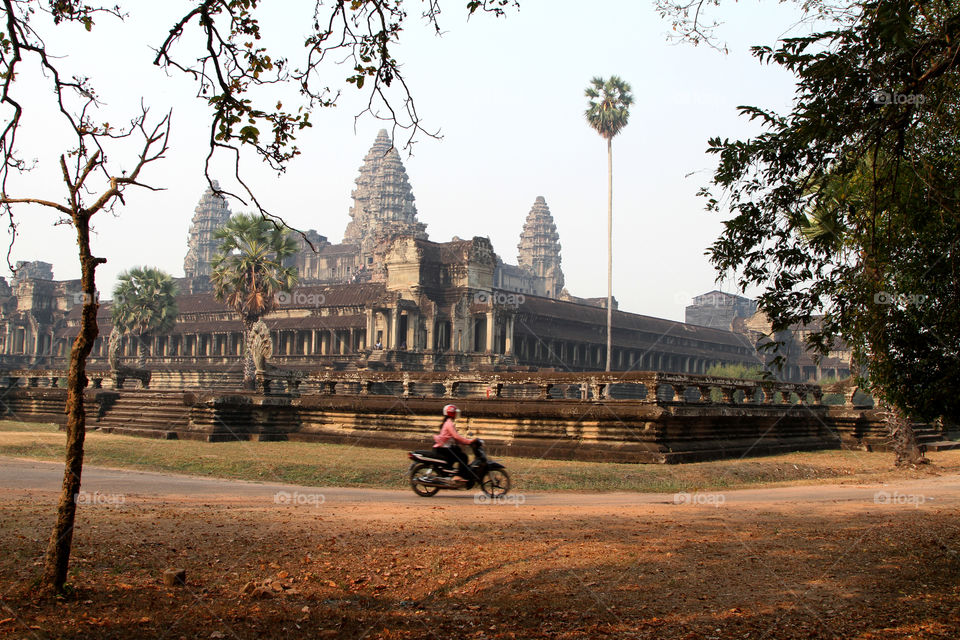 A woman rides a moped past the Angkor Wat temple complex in Cambodia
