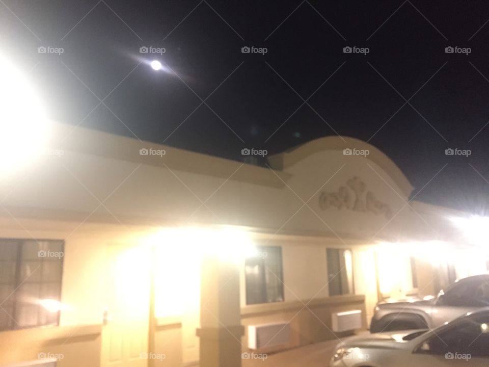 Moon in the night sky behind an adobe finished building. The moon is projecting beautiful rays of light in this photo.