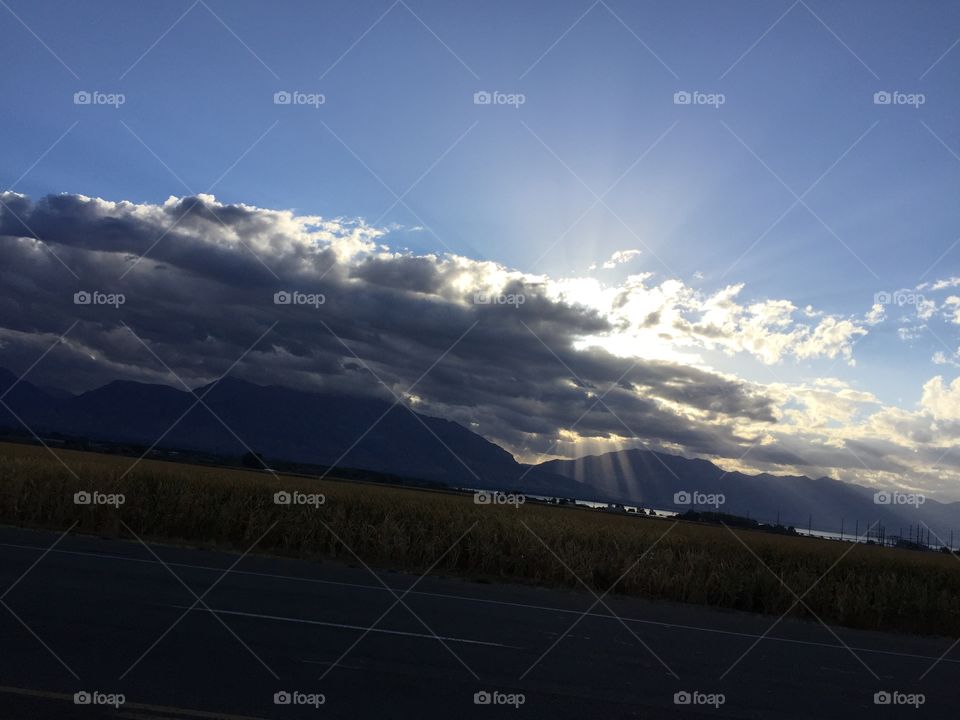 Sun rays through clouds over mountains over lake