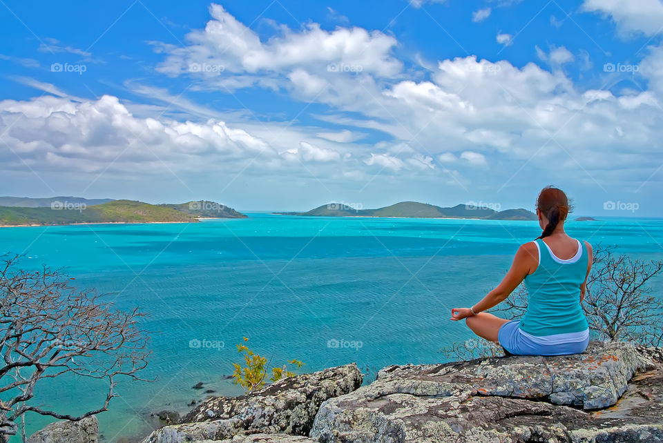 a woman meditating on a rock with beautiful ocean view