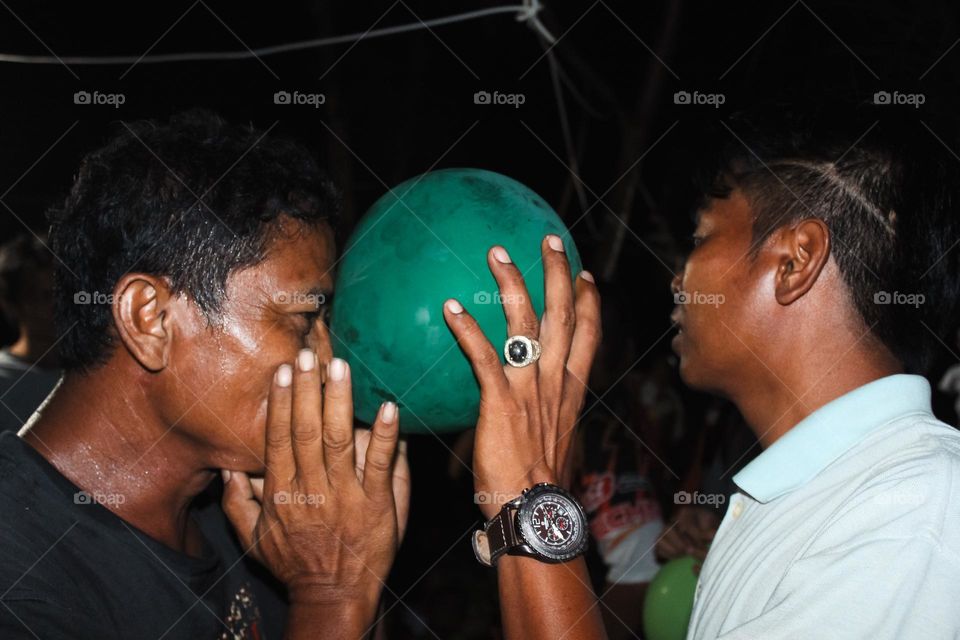 Close up of a group of men looking happy doing a dance game with balloons attached to their heads, a teamwork game to build a great team.