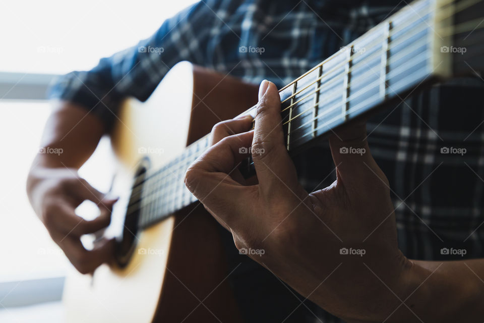 Close up men wearing blue plaid shirt playing guitar