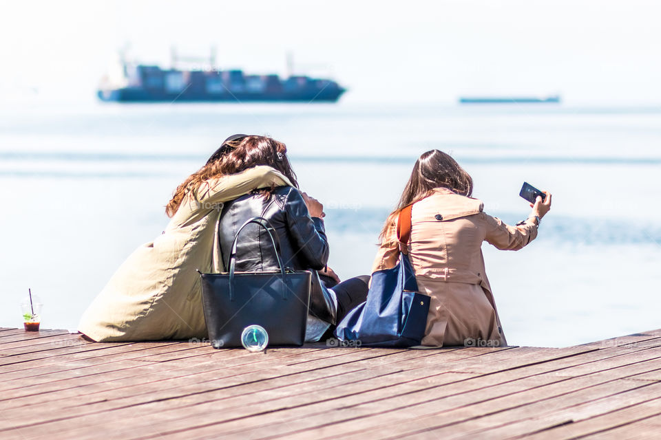 Young Girls Friends Taking Selfie And Using Mobile Phones At The Dock
