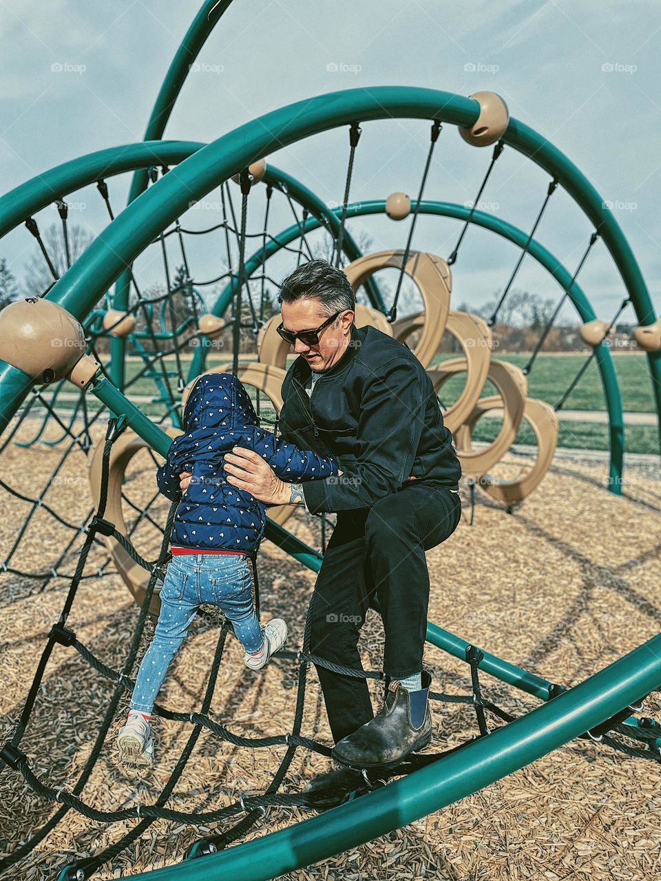 Dad helps child on playground, father figure plays with child, making memories with your kids at the park, dad has fun with toddler at the park, climbing on the playground equipment