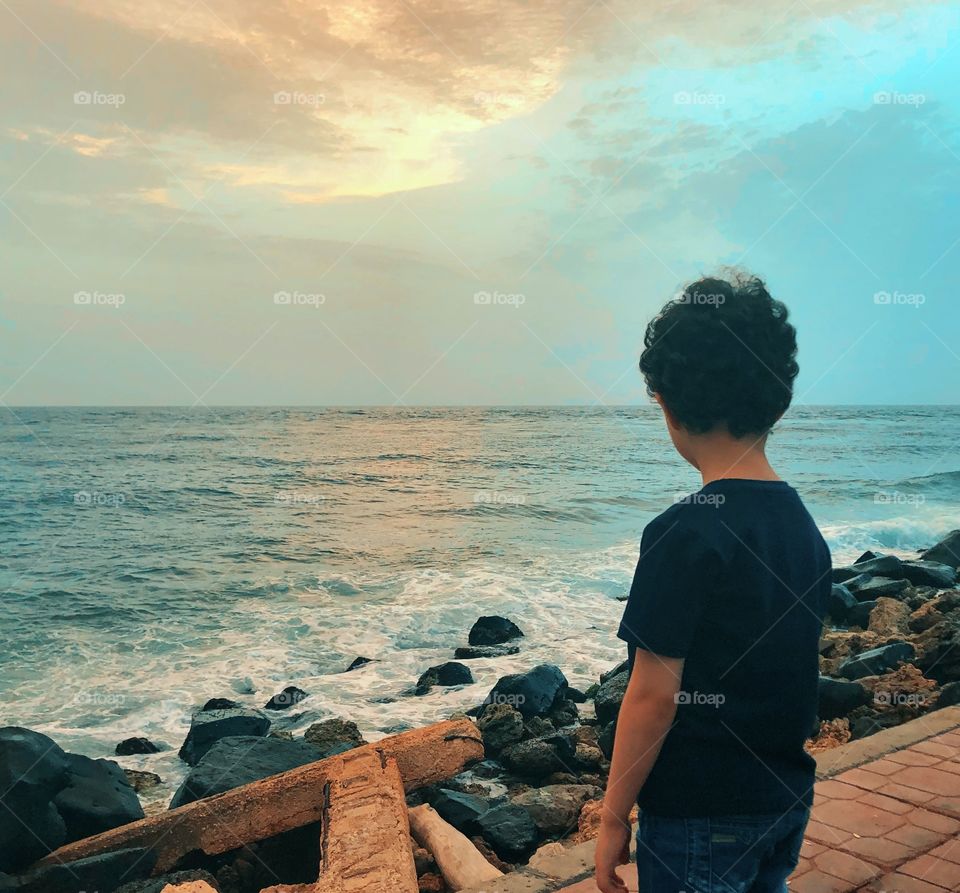 Little boy watching the sunset on seashore 