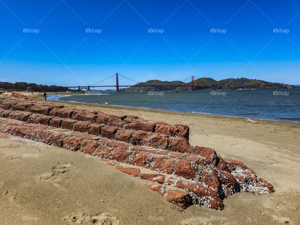 View of the Golden Gate Bridge from the beach at Crissy Field in San Francisco California, beautiful remnant of a brick wall in the foreground with soft sand and calm surf on a stunning warm clear day