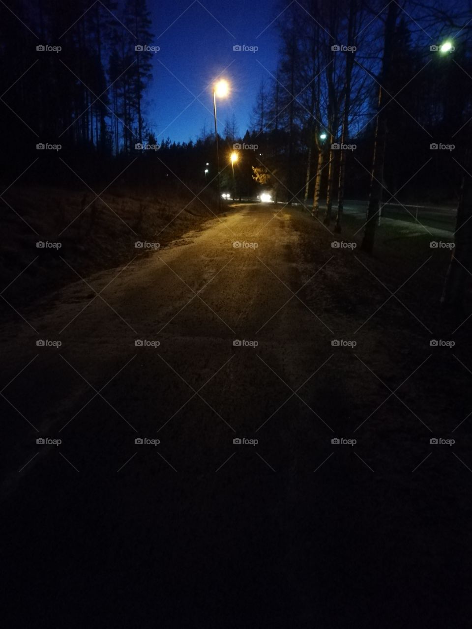 An icy road in the sunset. The lights of the streetlights and the cars are bright. The sidewalk is snowy in the dark evening.