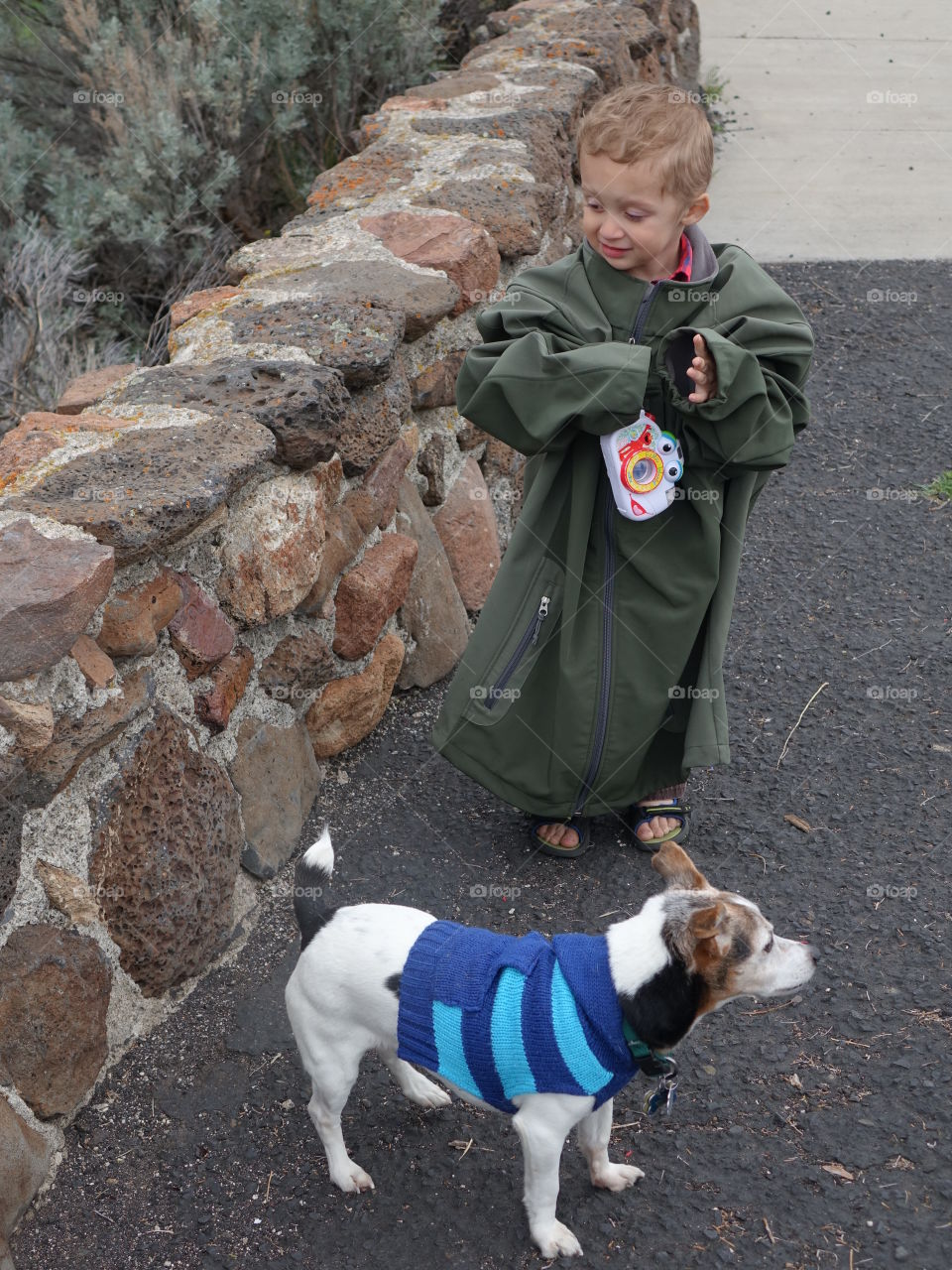 A cute little boy with his toy camera draped in an adult coat with his little Jack Russell Terrier adorned with a sweater in Central Oregon on a chilly spring day. 