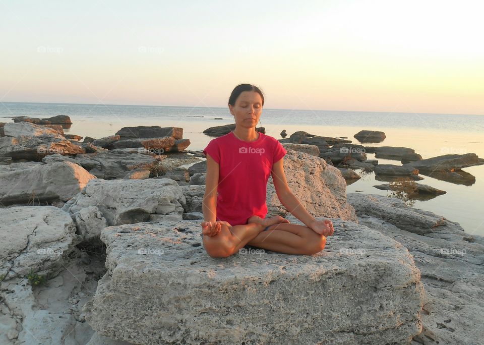 girl meditation in the yoga lotus pose on a sunset sea stone shore