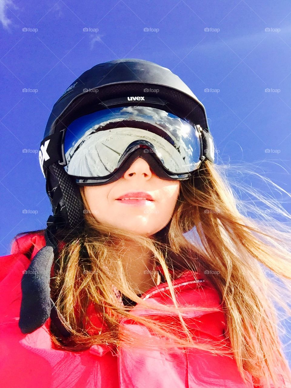 Portrait of woman wearing Uvex ski helmet and Uvex ski glasses with snow reflecting in the ski glasses and with blue sky above