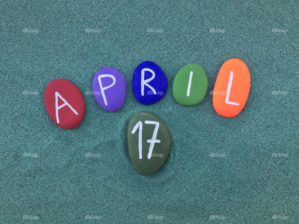 17 April, calendar date with colored stones over green sand 