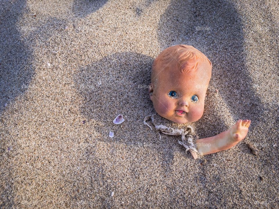 A doll waving hi from deep in the sand