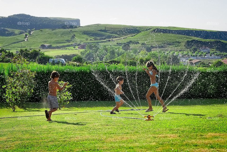 three children play with a sprinkler in summer
