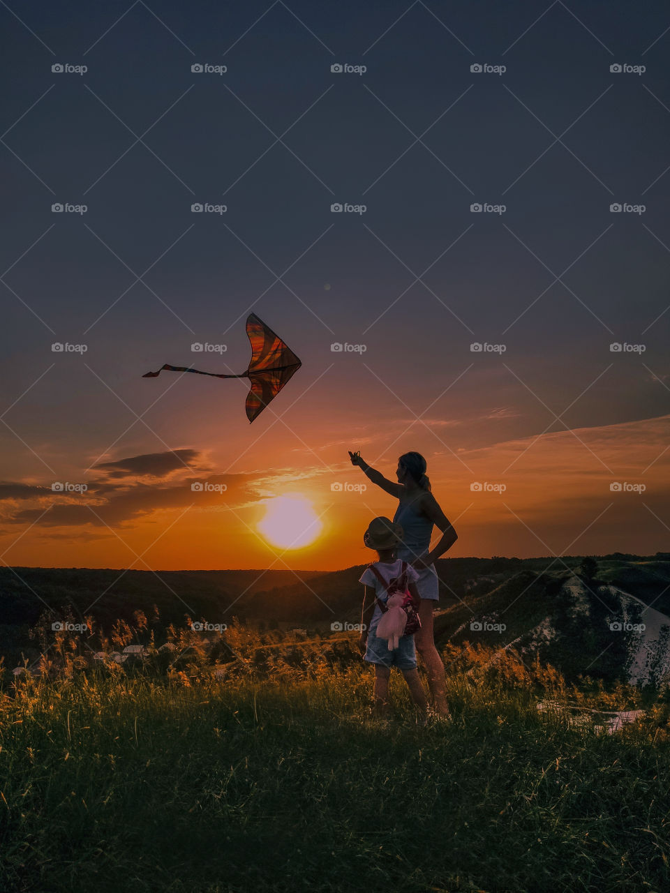 A child and his mother fly a kite at sunset