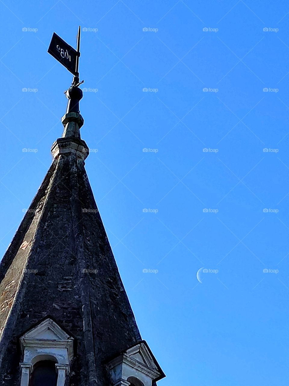 A blue sky with a white crescent moon.  In the foreground is the dome of the old tower.  sunny day
