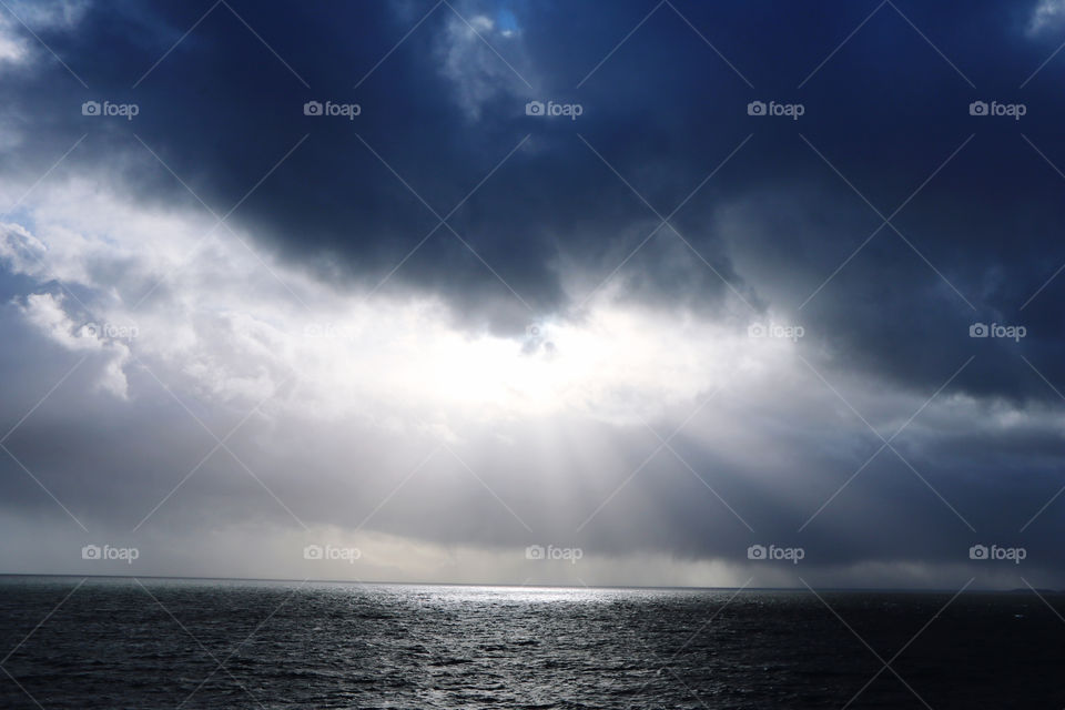 Dark clouds on the sky , yet the sun rays coming out through a hole  enlightening the ocean 