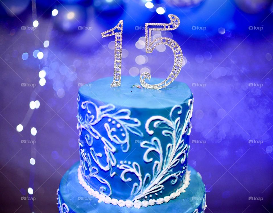 A number 15 atop a blue cake with white details 