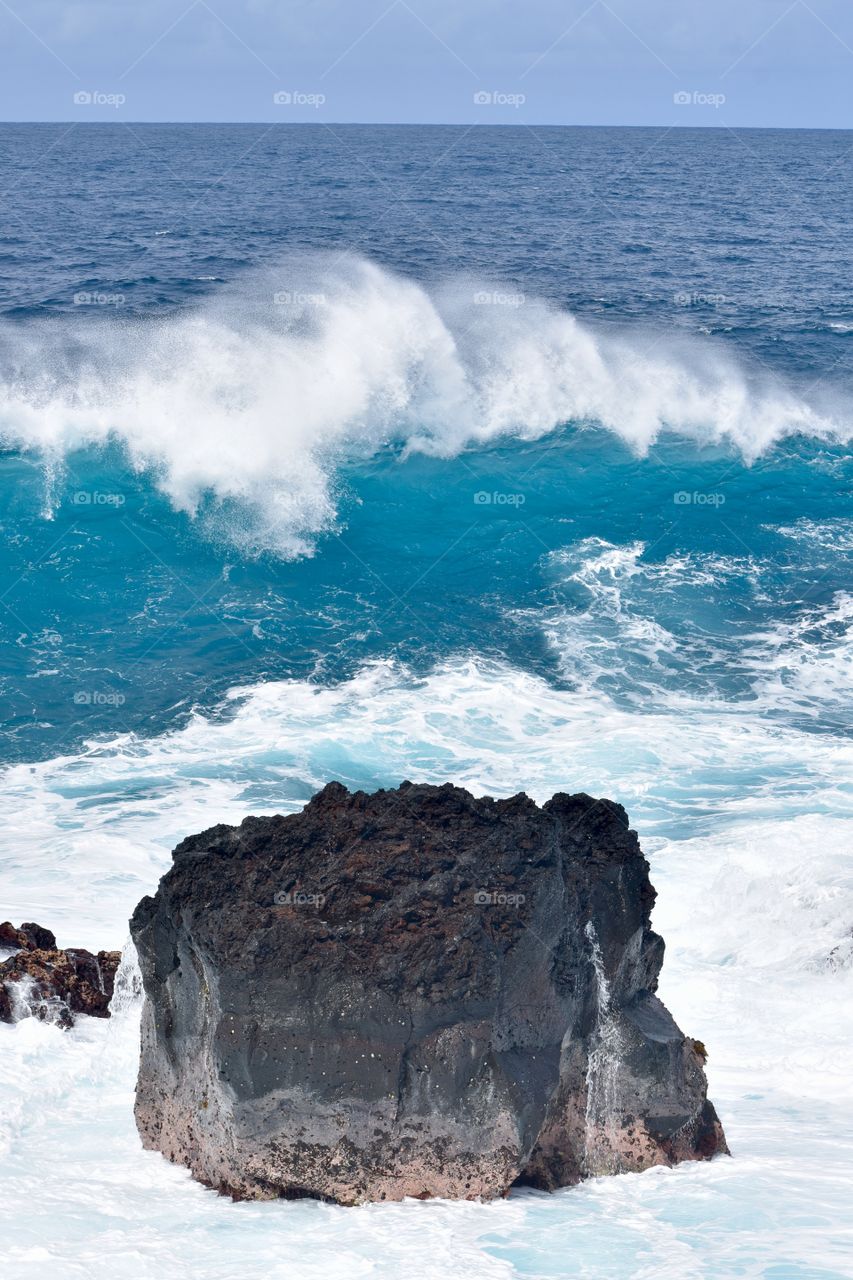 Big wave headed to the shore and the large lava rock in between.