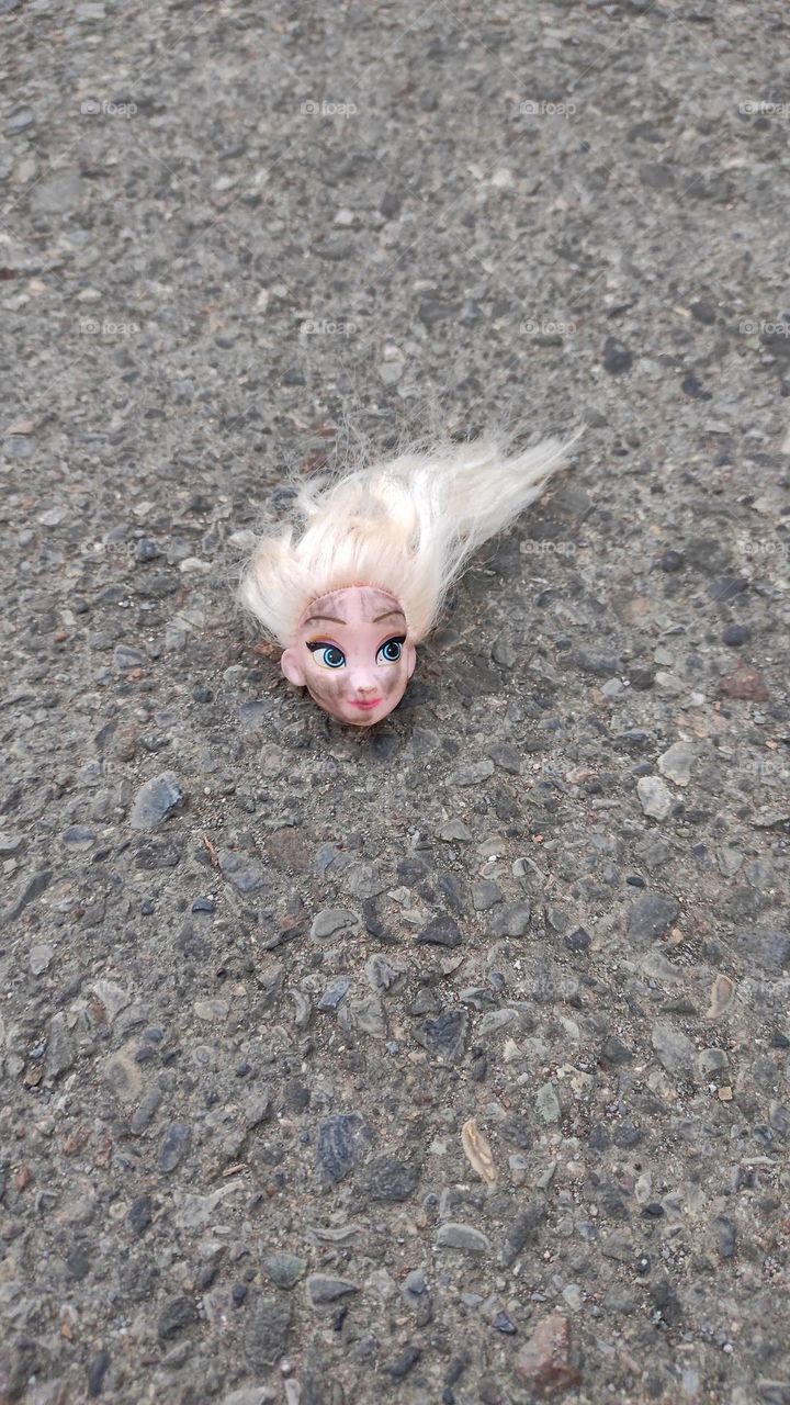 A blondish barbie doll's head without body on the ground.