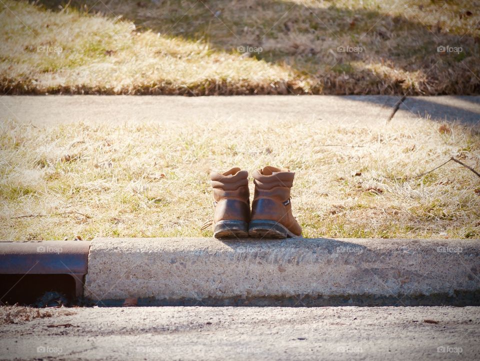 A man’s boots sit on the edge of the road, waiting for their owner to come back home. Were they forgotten?