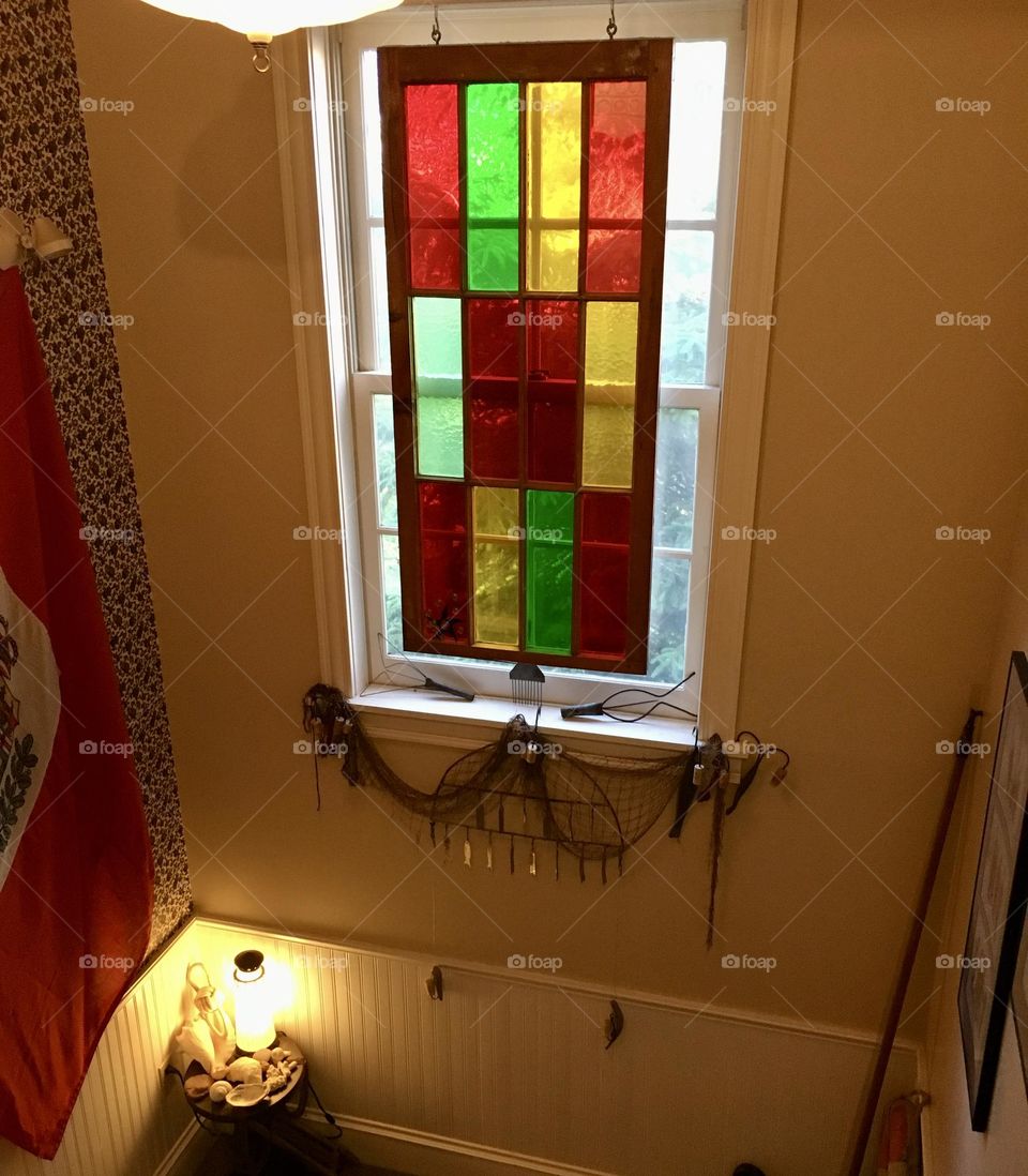 A cozy hallway between floors in a charming bed and breakfast on Prince Edward Island, where the coastal vibe of the island is reflected in every detail-with a stunning stained glass piece hanging over the window, and charming fish and shell decor.