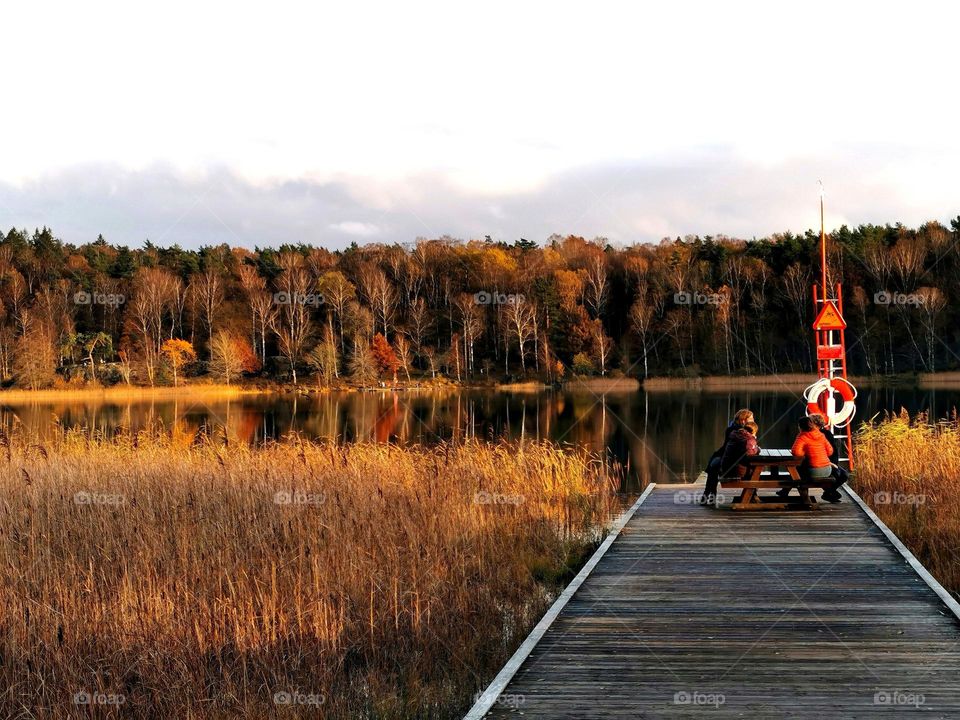 Autumn by the lake. People sitting  and talking at sunset.